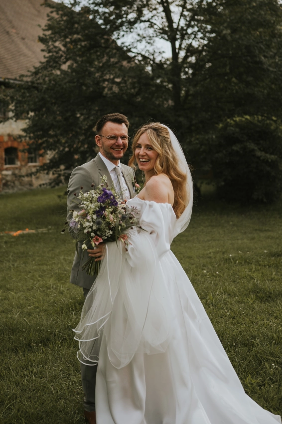 Brautpaar mit einem Brautstrauss aus Wildblumen bei ihrer luxuriösen Gartenhochzeit mit exklusiver Hochzeitpapeterie