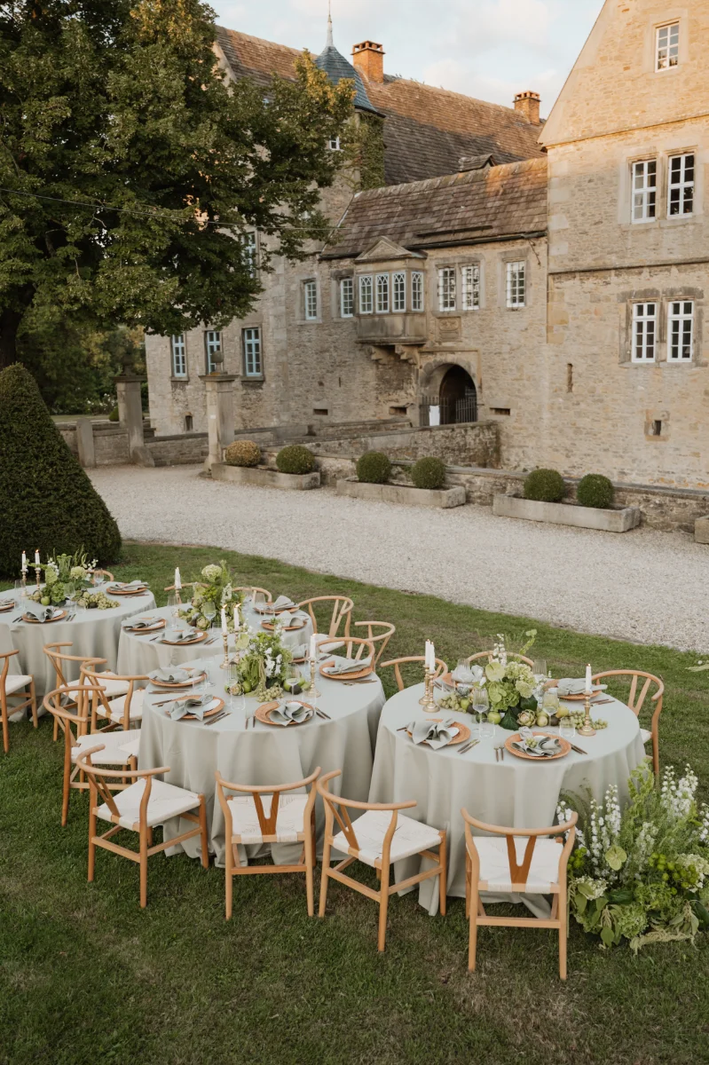 Elegante Outdoor-Hochzeit an einer historischen Schlosslocation mit stilvoll gedeckten Tischen in Grün- und Naturtönen – inspirierendes Setting für exklusive, moderne Hochzeitspapeterie und harmonisch abgestimmte Hochzeitskollektionen.